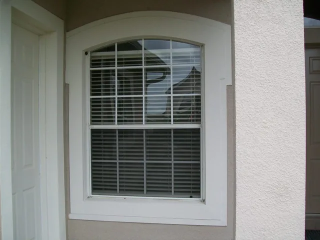 White-framed arched window with a grid pattern beside an entry.