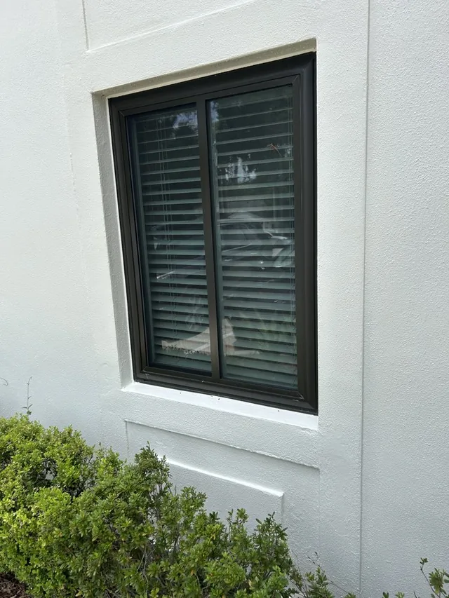 Dark-framed window with interior blinds on a light stucco wall.