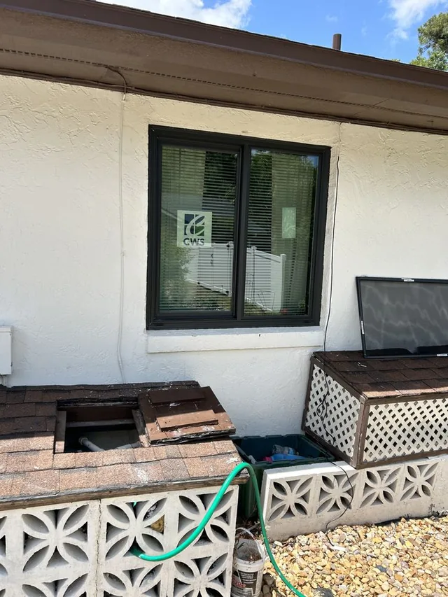 Dark-framed window with product labels above outdoor utility covers.