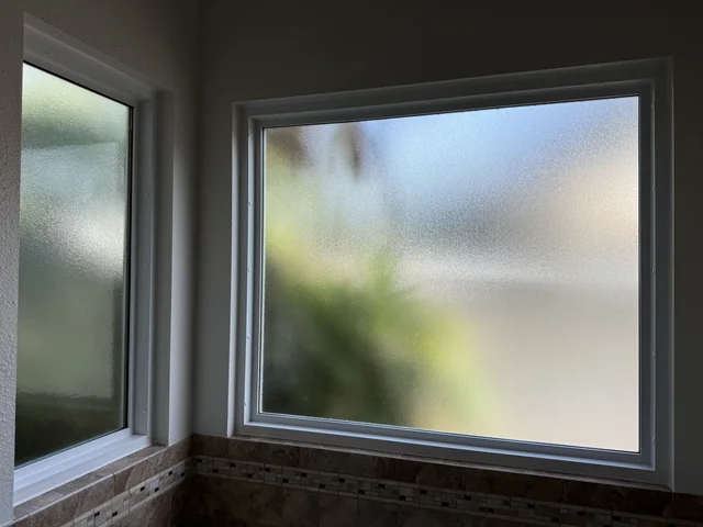 Two replacement privacy-glass windows with white frames in a tiled corner of the home.