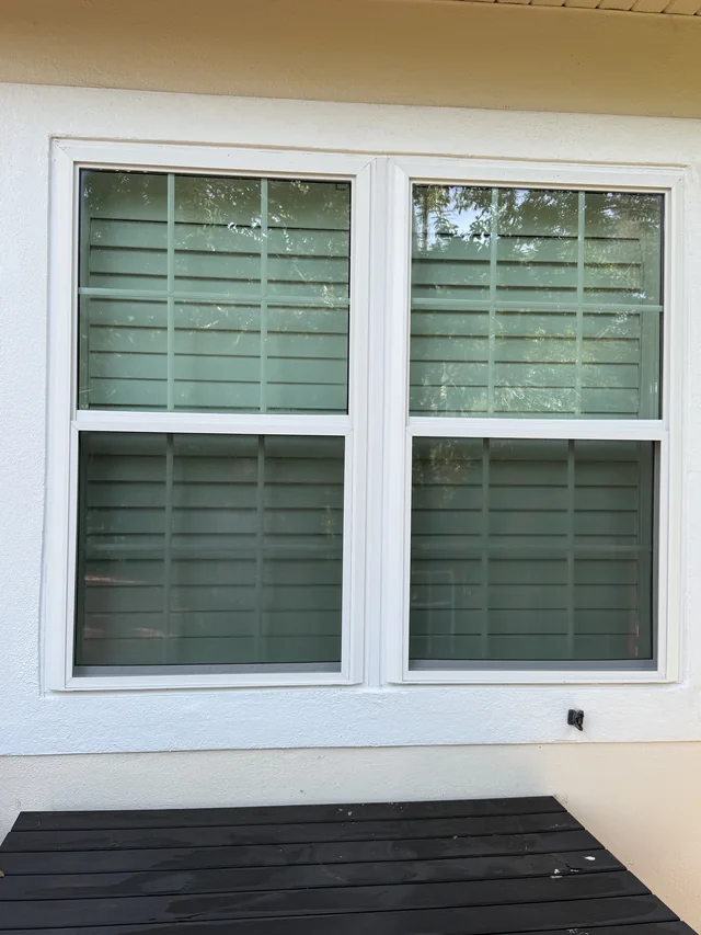 Pair of white-framed replacement windows with grids above an outdoor table on the patio.
