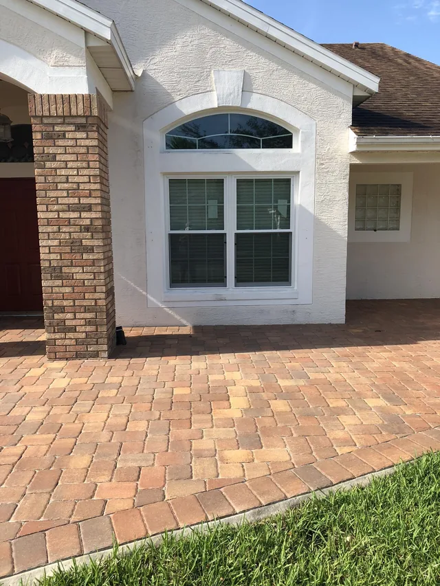 Two white-framed windows with grids below an arched transom beside a brick entry column.