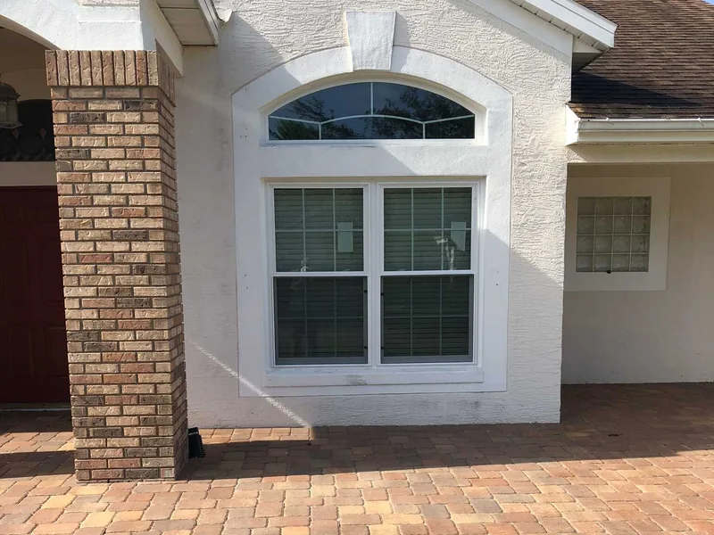 Paired white grid windows below an arched transom beside a brick entry in a Colonial project