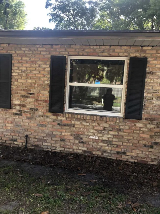 White-framed window between black shutters on a brick home exterior.