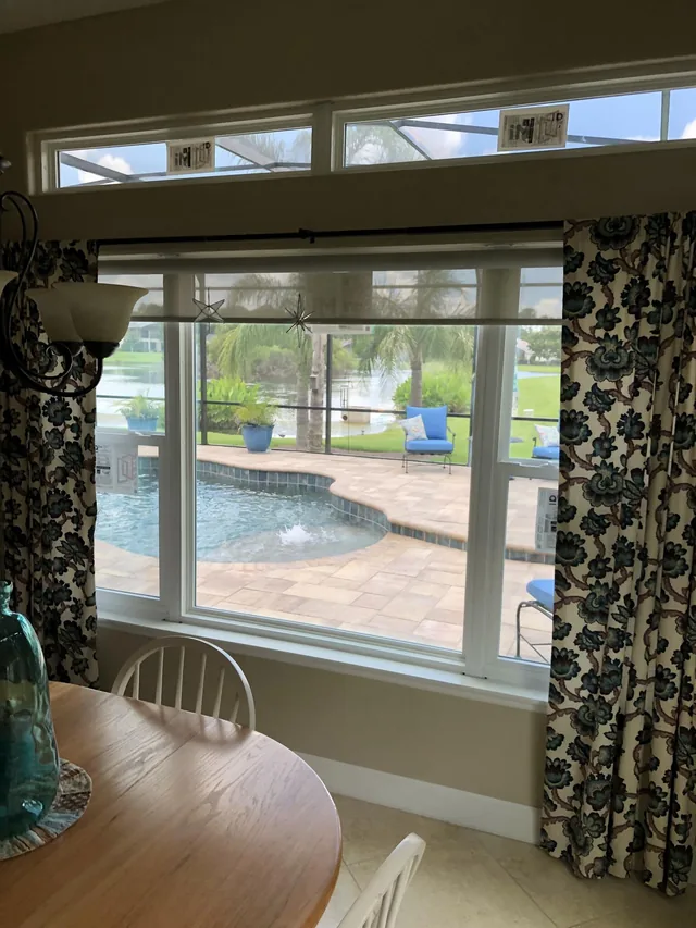 Interior view through a broad picture window and transoms toward a screened pool and lake.