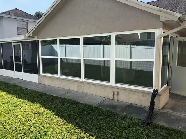 A row of white-framed windows wrapping around a sunroom beside a screened patio.