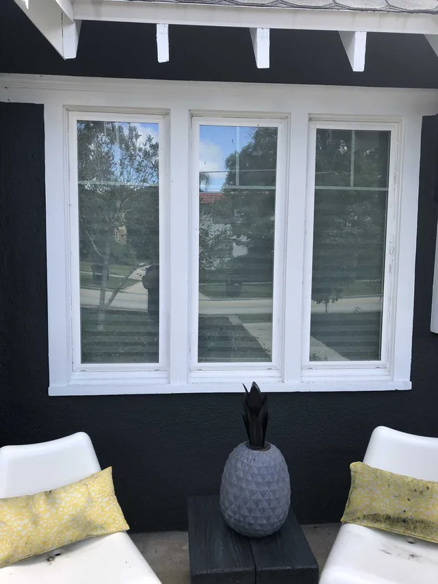 Three tall white-framed windows on a dark porch wall above chairs with pale cushions.
