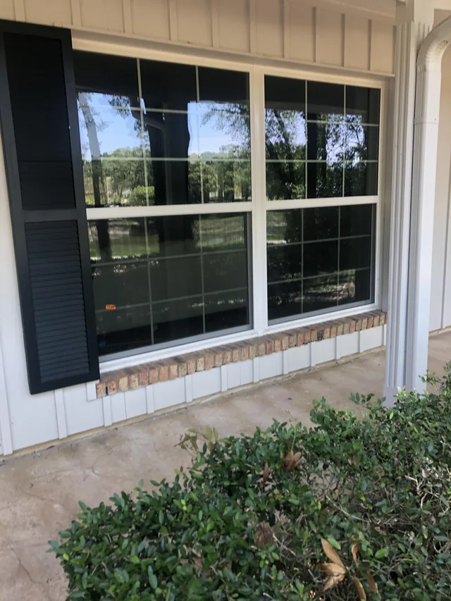 Two white-framed windows with grids above a brick sill on a covered porch.