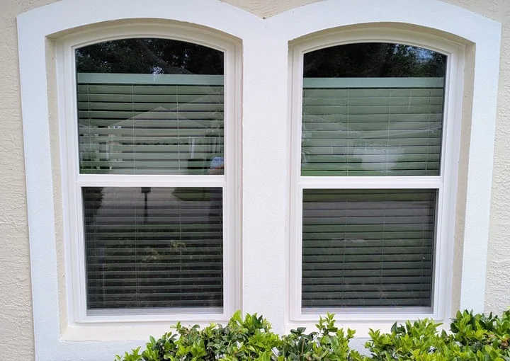 Two white single hung windows with arched tops in a stucco wall